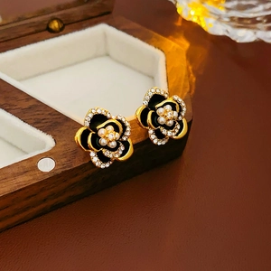 Detail view of gold flower earrings with black petals and pearls on a wooden box