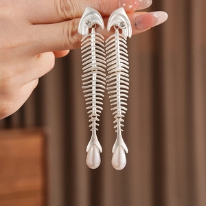 Macro detail of silver fishbone earrings featuring zircon head and drop pearl pendant