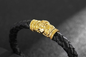 Close-up of golden embossed skull charms on black braided leather bracelet with magnetic clasp