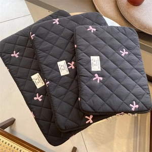 Detail shot of black quilted laptop sleeve with cute pink bow embroidery and woven label.