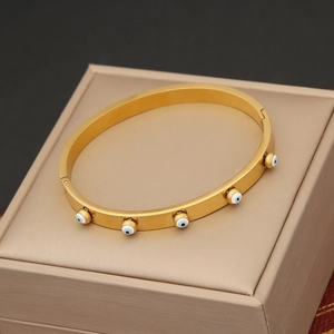 Detailed shot of a gold oval bangle with blue evil eye charms on a luxury jewelry box