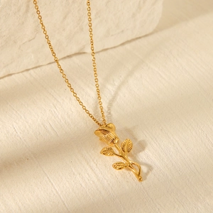 Close-up of golden rose pendant necklace featuring detailed petals on a beige stone surface