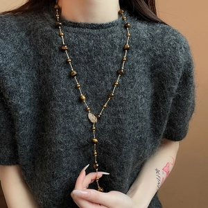 Detailed view of leaf pendant necklace with tiger eye beads on grey sweater