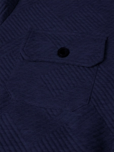 Detail of navy textured quilted fabric with a black button on the men's jacket pocket