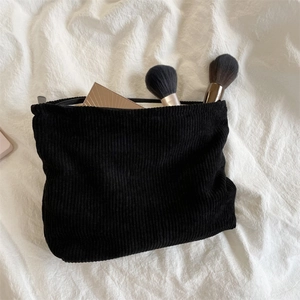 Minimalist black corduroy makeup bag placed on a white pleated fabric surface