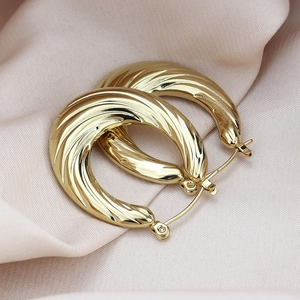Detailed view of golden croissant hoop earrings resting on soft pink silk fabric