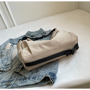 Detailed close-up of a beige canvas tote bag with adjustable black strap on denim jacket