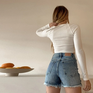 Top bianco a maniche lunghe con ritagli e pantaloncini di jeans visti dal retro