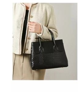 Detail of black tote handbag featuring crocodile pattern texture and premium synthetic leather