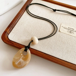 Close-up of amber resin teardrop pendant with cream bead on black cord over linen