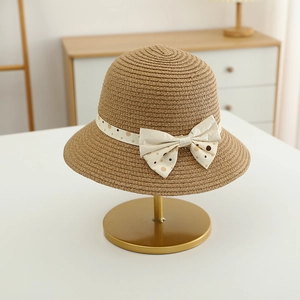 Close-up of children straw sun hat featuring a cream polka dot bow on a metal stand