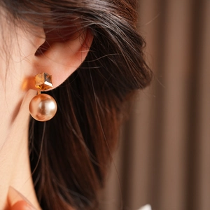 Close-up of elegant gold geometric cube earring with a large drop pearl on a model