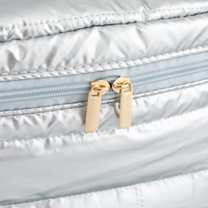Close-up of metallic quilted fabric with premium dual gold zippers on a silver makeup bag