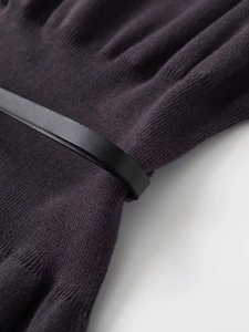 Detail of fine dark knit fabric texture with a slim black leather belt and soft pleats