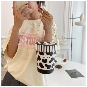 Detail of cow print milk cup bucket bag with gold chain strap on a model shoulder
