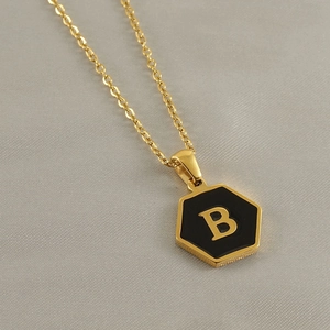 Detail of a gold stainless steel hexagonal pendant with black enamel and gold letter B