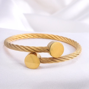 Minimalist gold-plated stainless steel cable bracelet with circular flat ends on fabric
