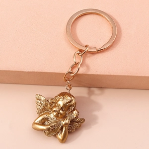 Detail of golden relief angel keychain holding a lyre on an apricot background