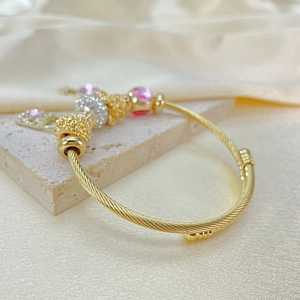 Close-up of golden beaded bracelet with pink heart pendant on marble and silk background