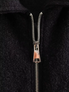 Detailed macro view of the silver metal zipper on the black wool blend jacket fabric