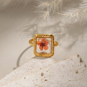 Macro detail of golden square ring with dried flower specimen on stone texture