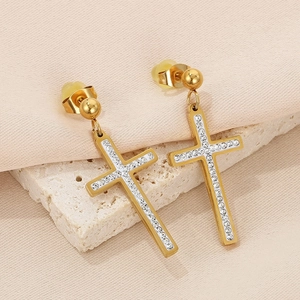 Close-up of golden cross earrings with zircon crystals on a textured stone surface