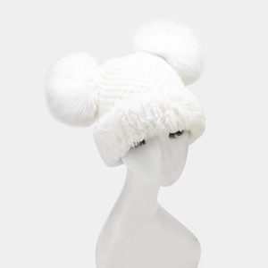 Detail of white knit winter hat featuring twin faux fur pom-poms and plush ear flaps