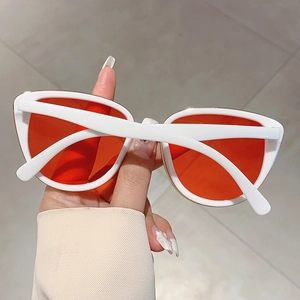 Detail of white cat-eye sunglasses with orange lenses and elegant gold metal trim accents