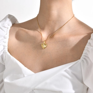 Primo piano di una collana con ciondolo a cuore dorato con trama a raggiera su modella