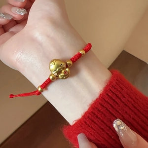 Détail du bracelet corde rouge porte-bonheur avec pendentif doré sur le poignet