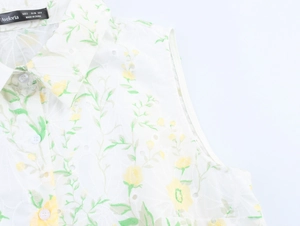 Dettaglio del ricamo floreale e tessuto traforato su camicia bianca senza maniche