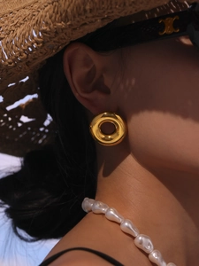 Close-up of golden chunky hoop earrings and baroque pearl necklace on a model