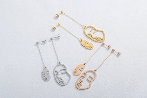 Détail des boucles d'oreilles visage abstrait en finitions or, argent et or rose poli