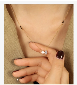 Detail of a minimalist gold necklace with double teardrop pendants and black beads