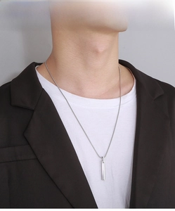Close-up of a men's silver cylinder bar pendant with thin snake chain on a model