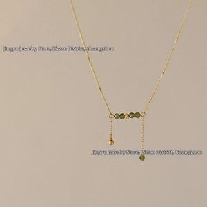 Close-up of golden necklace with olive green faceted beads and double tassel charms