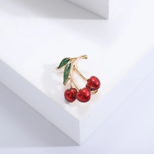 Elegant red enamel cherry brooch with green leaves and gold stem on white background