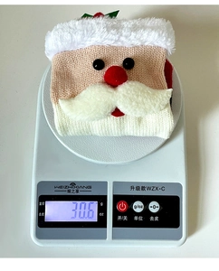 Weight detail of knitted Santa Claus wine bottle cover with white beard on digital scale
