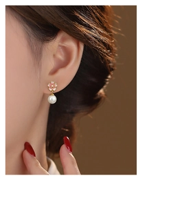 Close-up of pink cherry blossom earrings with pearl drop on ear showing elegant gold details