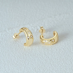 Macro detail of gold C-shaped earrings with embossed stars and tiny clear zircons