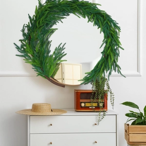 Detail view of a round mirror framed with lush green artificial Norfolk pine branches