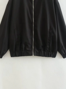Detail of black bomber jacket with silver zipper, elastic hem and side slash pockets