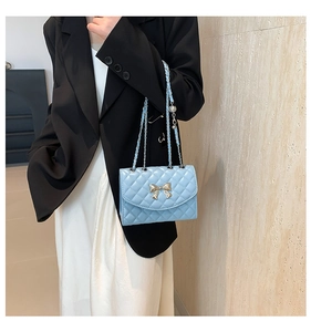 Detail of light blue quilted crossbody bag with gold bow clasp and chain strap