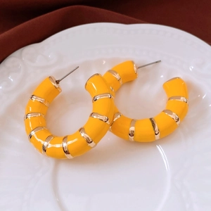 Macro shot of yellow enamel hoop earrings with gold metal stripes on white tray