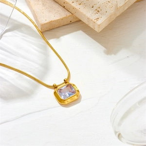 Macro shot of gold snake chain with emerald cut zircon pendant on a textured background