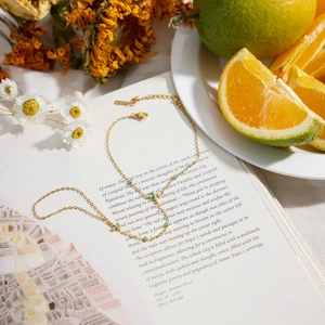 Elegantes Goldkettenarmband mit Türkisperlen und Metallkugeln auf einem Buchhintergrund