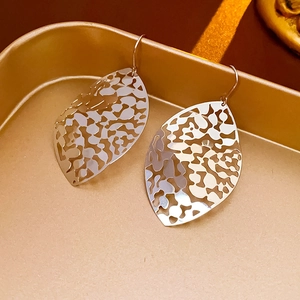 Detailed close-up of silver hollow leaf earrings on a decorative golden tray