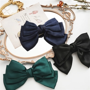 Three-layer satin bow hair clips in navy, black, and green on a vintage scene background