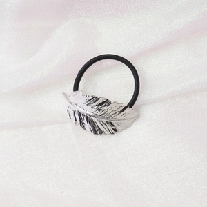 Detail of silver feather metal ornament on black elastic hair tie over white silk