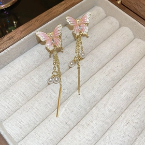 Détail de boucles d'oreilles papillon dorées avec émail rose et perles sur support bois